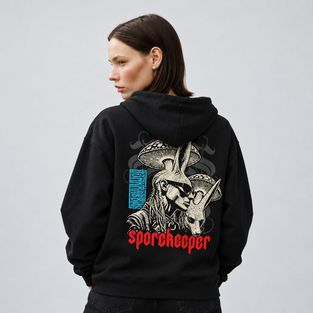 Mara wearing the black Spore Keeper hoodie, back view showing a rabbit-eared human in dark glasses beside a rabbit head under mushroom caps, with red Sporekeeper lettering.
