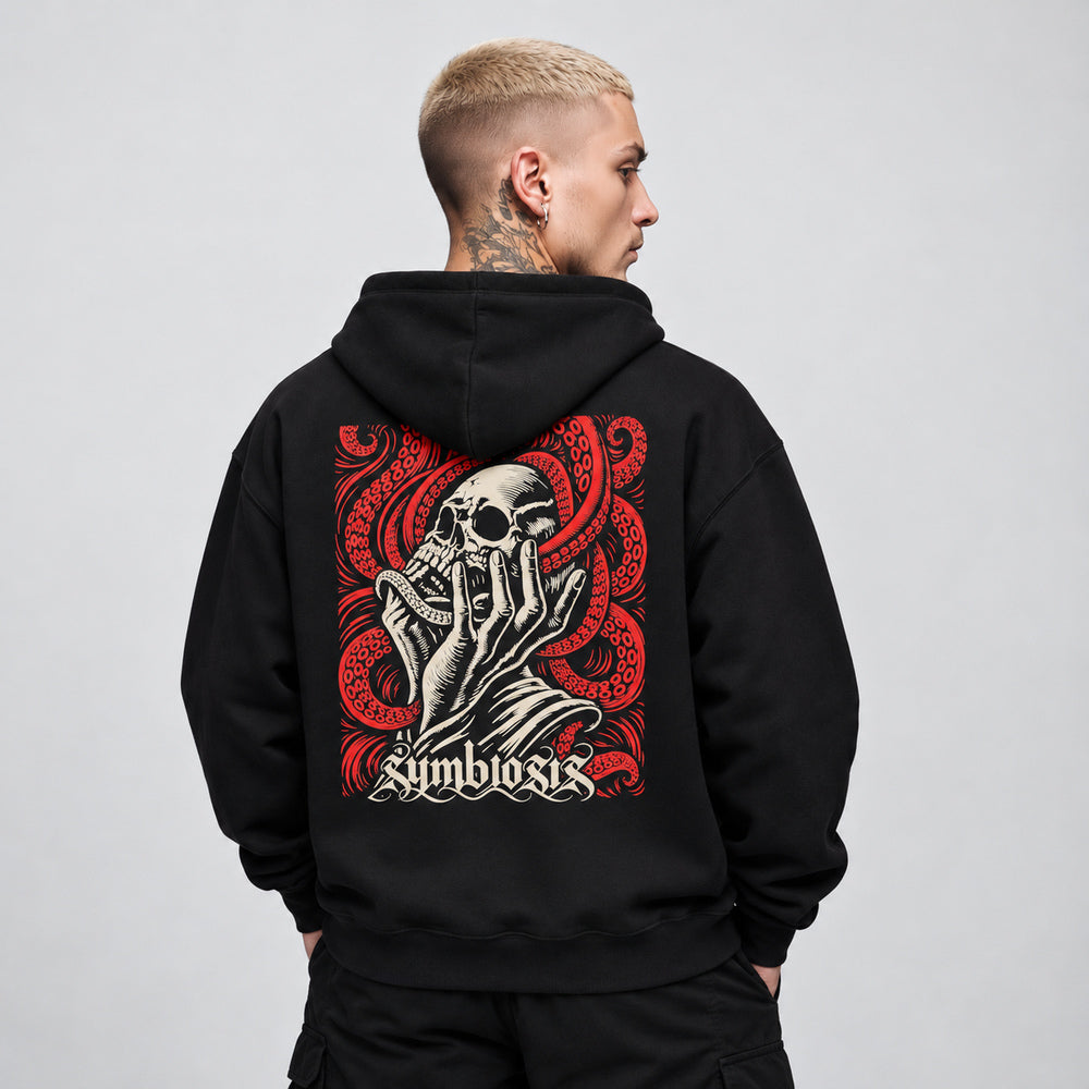 James wearing the black Symbiosis hoodie, back view showing an ivory skull cradled by an upward-reaching hand amid red octopus tentacles with suction cups, with ivory Symbiosis lettering.