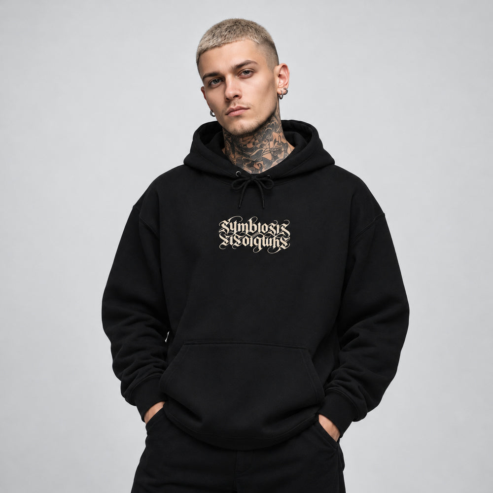 James wearing the black Symbiosis hoodie, front view showing paired upright and inverted ivory Symbiosis lettering.