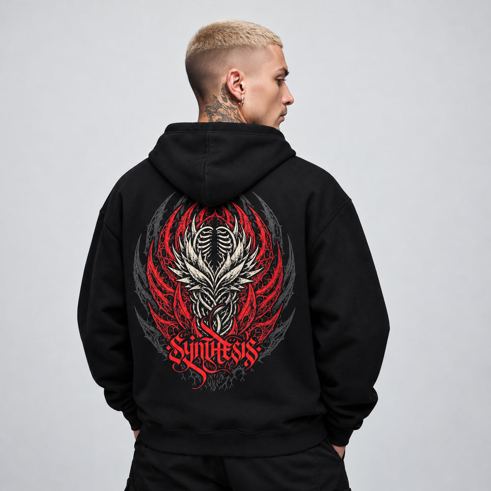James wearing the black Synthesis hoodie, back view showing an ivory ribcage and interwoven organic forms framed by red thorn-like curves and charcoal ornament, with red Synthesis lettering.