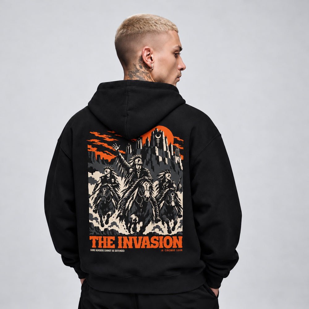 James wearing The Invasion black Gildan 18500 hoodie, back view with three masked horse riders charging below a fortress and orange sky