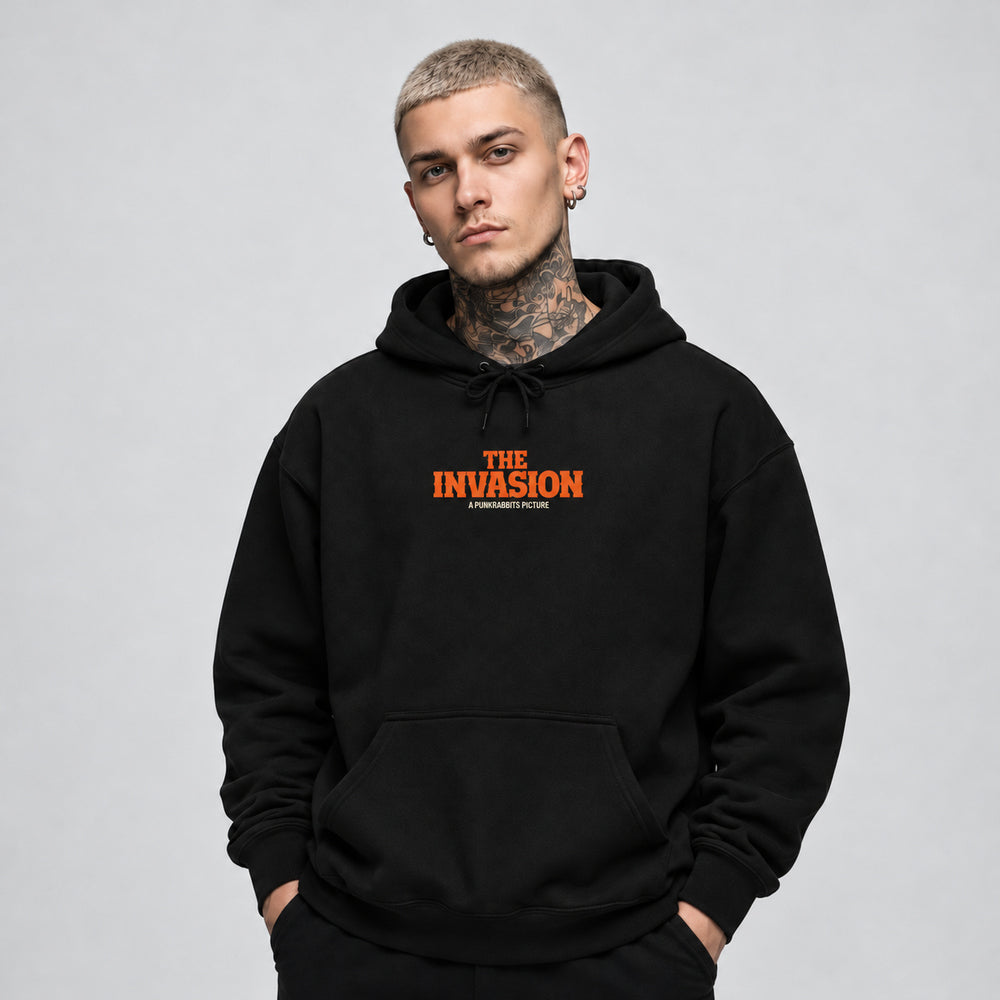 James wearing The Invasion black Gildan 18500 hoodie, front view with orange The Invasion chest lettering